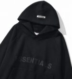 Black Essentials oversized hoodie with tonal chest logo, kangaroo pocket, and hood label, displayed on a white background in a modern streetwear style.